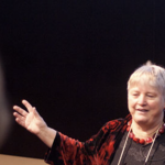 A presenter on a black background in front of an audience